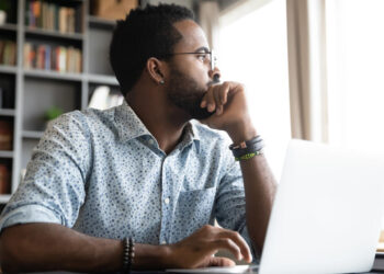 Thoughtful serious african professional business man sit with laptop thinking of difficult project challenge looking for problem solution searching creative ideas lost in thoughts at home office desk