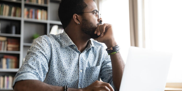 Thoughtful serious african professional business man sit with laptop thinking of difficult project challenge looking for problem solution searching creative ideas lost in thoughts at home office desk