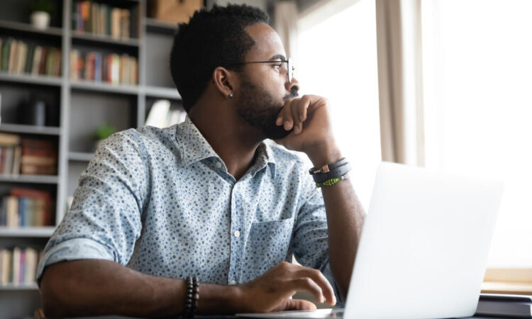 Thoughtful serious african professional business man sit with laptop thinking of difficult project challenge looking for problem solution searching creative ideas lost in thoughts at home office desk