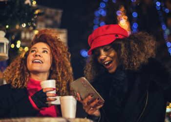 Young beautiful women drinking hot drinks and having fun at Christmas market during holiday shopping