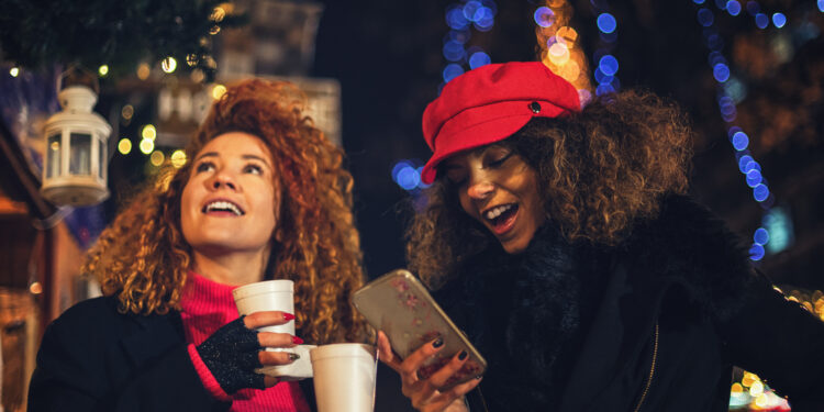 Young beautiful women drinking hot drinks and having fun at Christmas market during holiday shopping