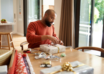 Shot of a young man wrapping Christmas presents at home