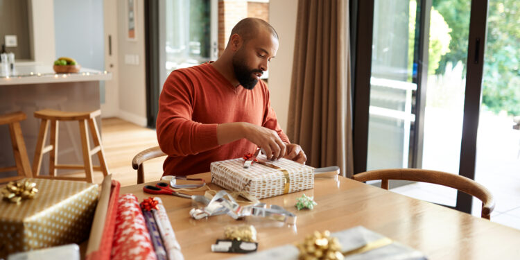 Shot of a young man wrapping Christmas presents at home