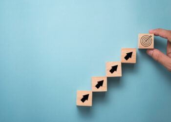 Hand putting virtual target board and arrow which print screen on wooden cube. Business achievement goal and objective target concept.